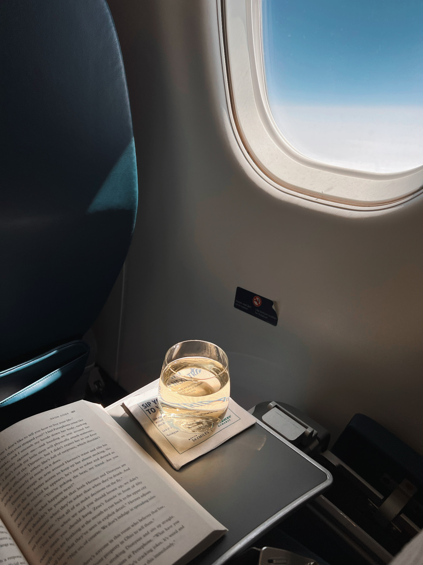 A glass of wine on a tray table beside an aircraft window